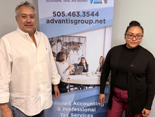 Luis is on the left, and a female employee is on the right, and in between is a stand up banner advertising Advantis Group Co. 