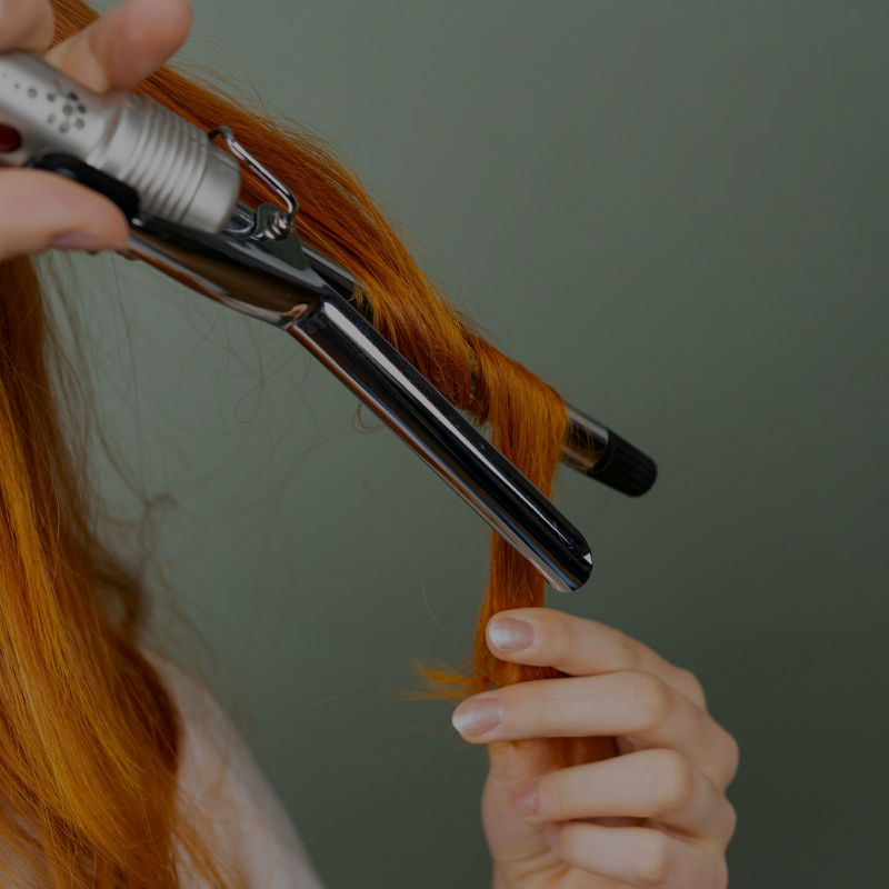 Woman with orange hair wrapping her own hair around curling iron