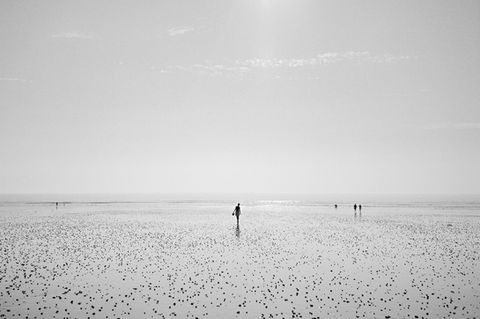 Une fille au loin sur le rivage brillant a une jolie silhouette, elle marche en tenant ses chaussures. Claude Pavelek