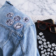 DENIM JACKET AND BLACK CLUTCH WITH FLORAL STICKERS AND PATCHES ON THEM.