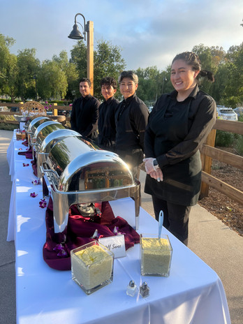 Catering staff standing behind a buffet line outdoors, ready for guests.