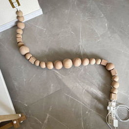 Wooden bead-covered electrical cable by BLESS on a grey stone floor