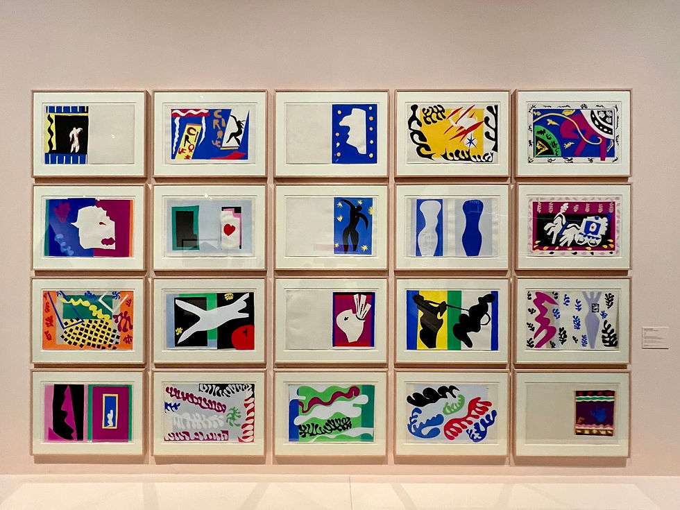 A wall displaying 16 colorful abstract artworks in a grid, featuring bold shapes and vibrant colors. No visible text. Bright and lively mood.