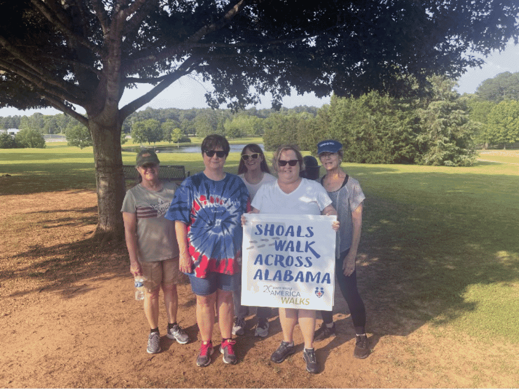 group of walkers standing under a tree holding a sign for Shoals Walk Across Alabama