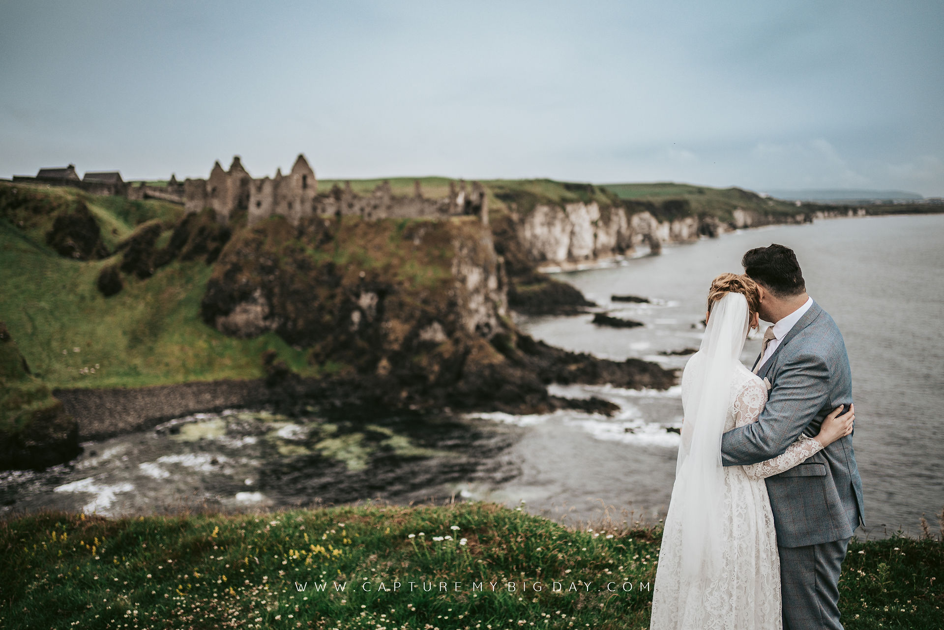 bride and groom with coastline behind them