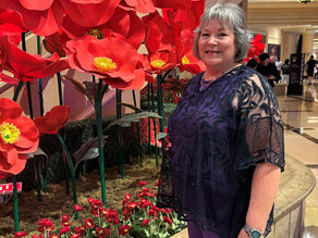 Image of Nancy Busey standing in front of a display of large, bright red, silk poppies.