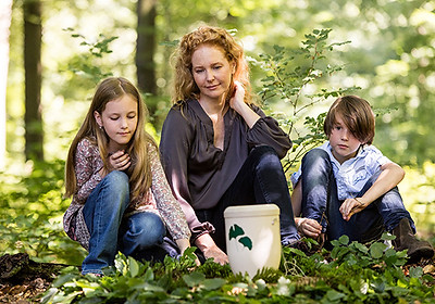 Eine Mutter und ihre zwei Kinder knien im Wald hinter einer weißen Urne.