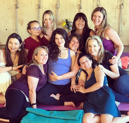 Aimee Takaya sits pregnant and holding her belly surrounded by a group of smiling womenand others