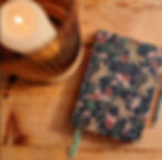 A close up of a candel and a floral notebook upon a wooden table.