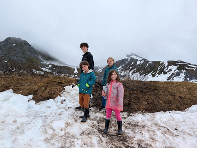 Four children standing on snowy ground along the Gold Cord Lake Trail in Hatcher Pass, Alaska, with misty mountains in the background