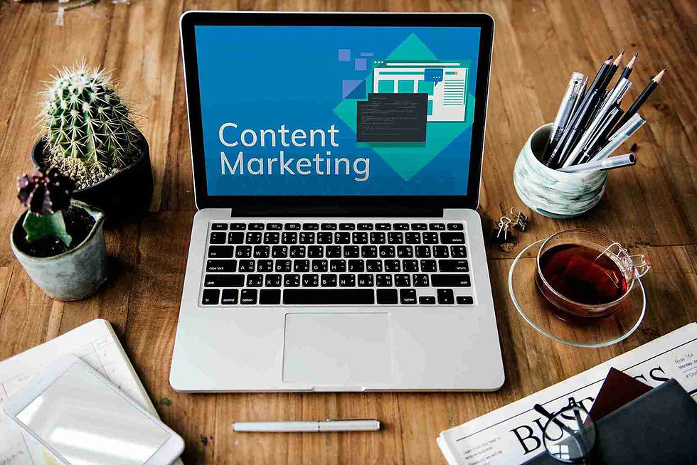A laptop on a wooden table displays "Content Marketing" on its screen. Nearby are a cactus, pens in a cup, tea, and a paper with "Business" text.