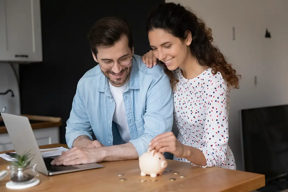 Smiling couple in a cozy room uses a laptop. Woman places a coin in a pink piggy bank on a wooden table. Light, cheerful atmosphere.
