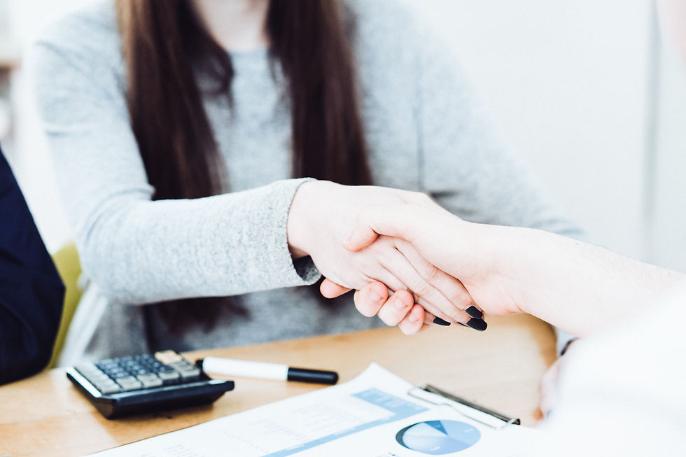 Two people shaking hands over a table with a pen, calculator, and documents. Bright setting with a cooperative mood.