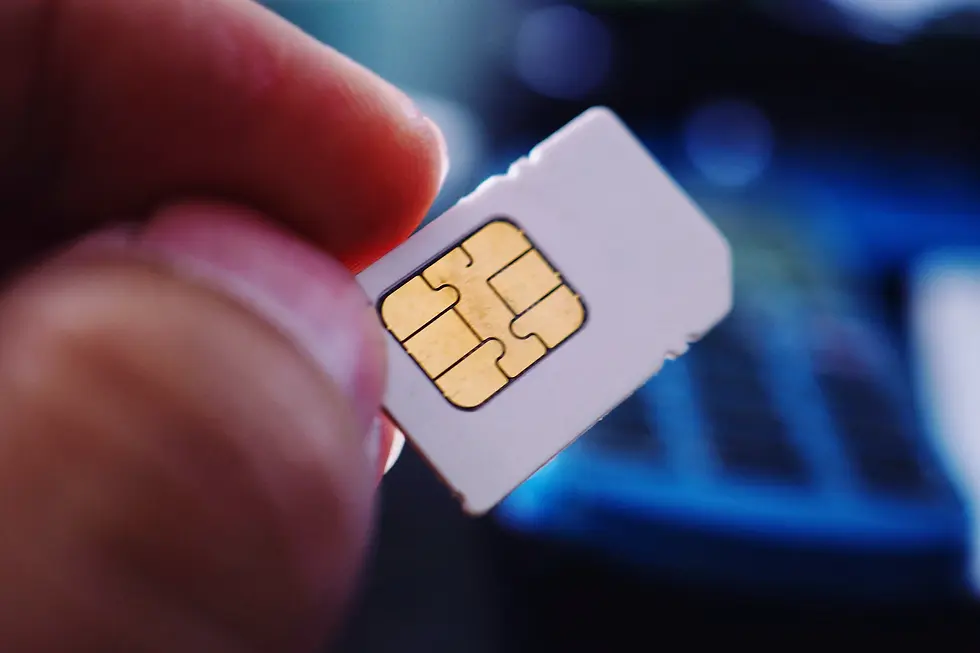 Close-up of a hand holding a SIM card with a gold chip. Blurred blue and black background, highlighting the card's details.