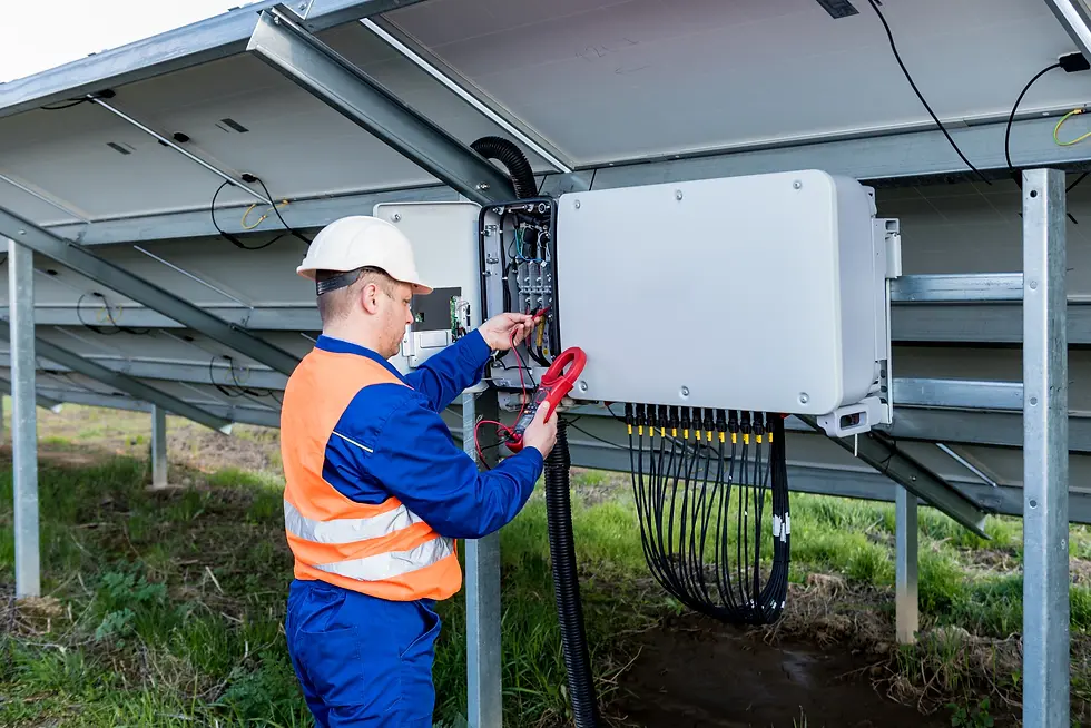 Worker in blue and orange gear, examines solar panel wiring outdoors. Wearing a helmet, he uses a multimeter on a control box.