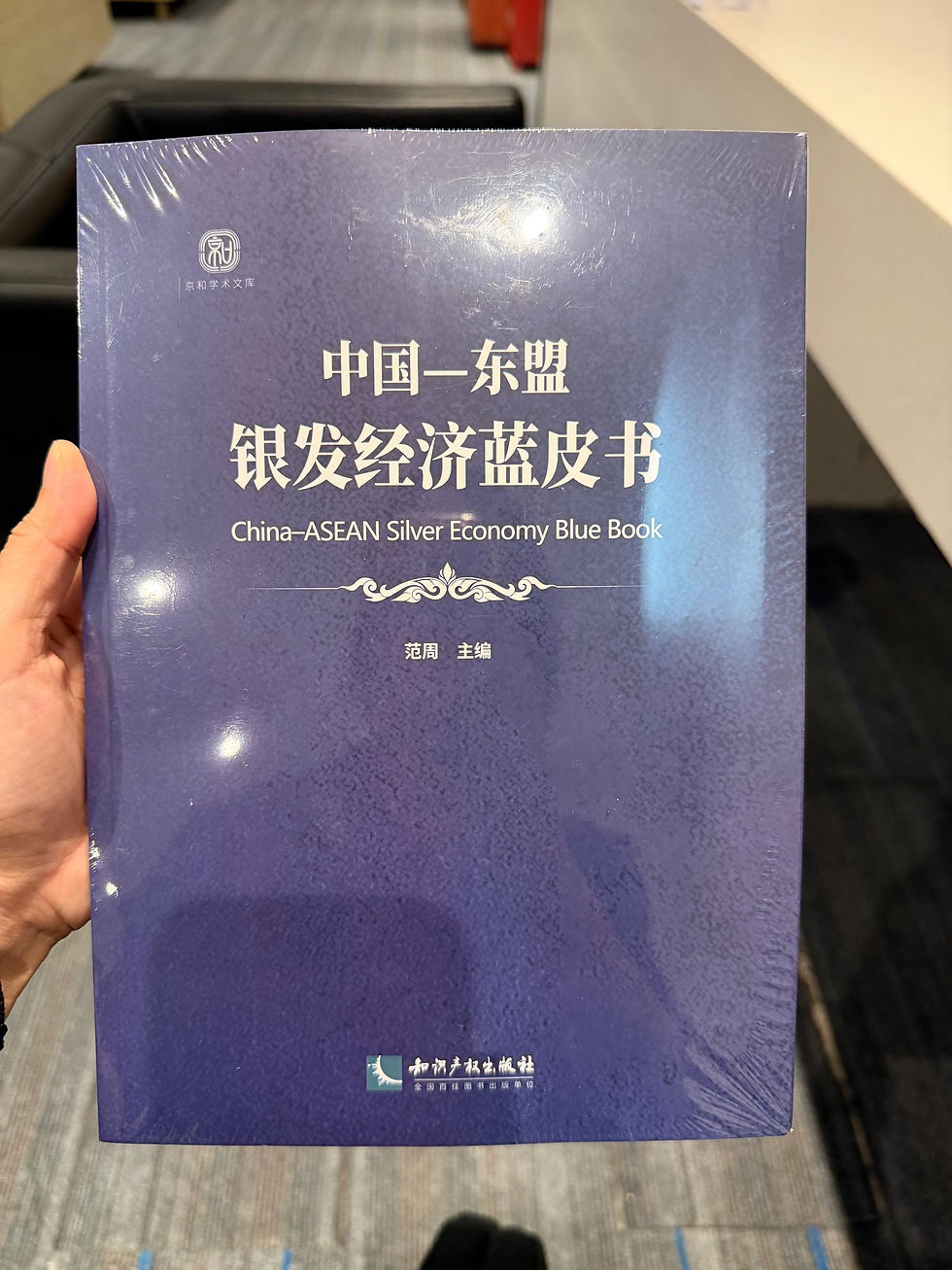 Hand holding a purple Chinese book titled China-ASEAN Silver Economy Blue Book in a quiet indoor setting.