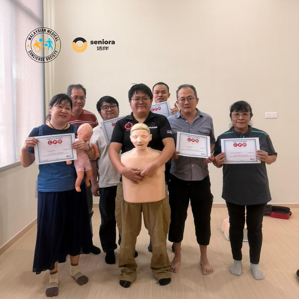 Seven people pose with certificates and a CPR mannequin in a bright room. Logos on the wall read "Malaysian Medical Concierge Society" and "Seniors".