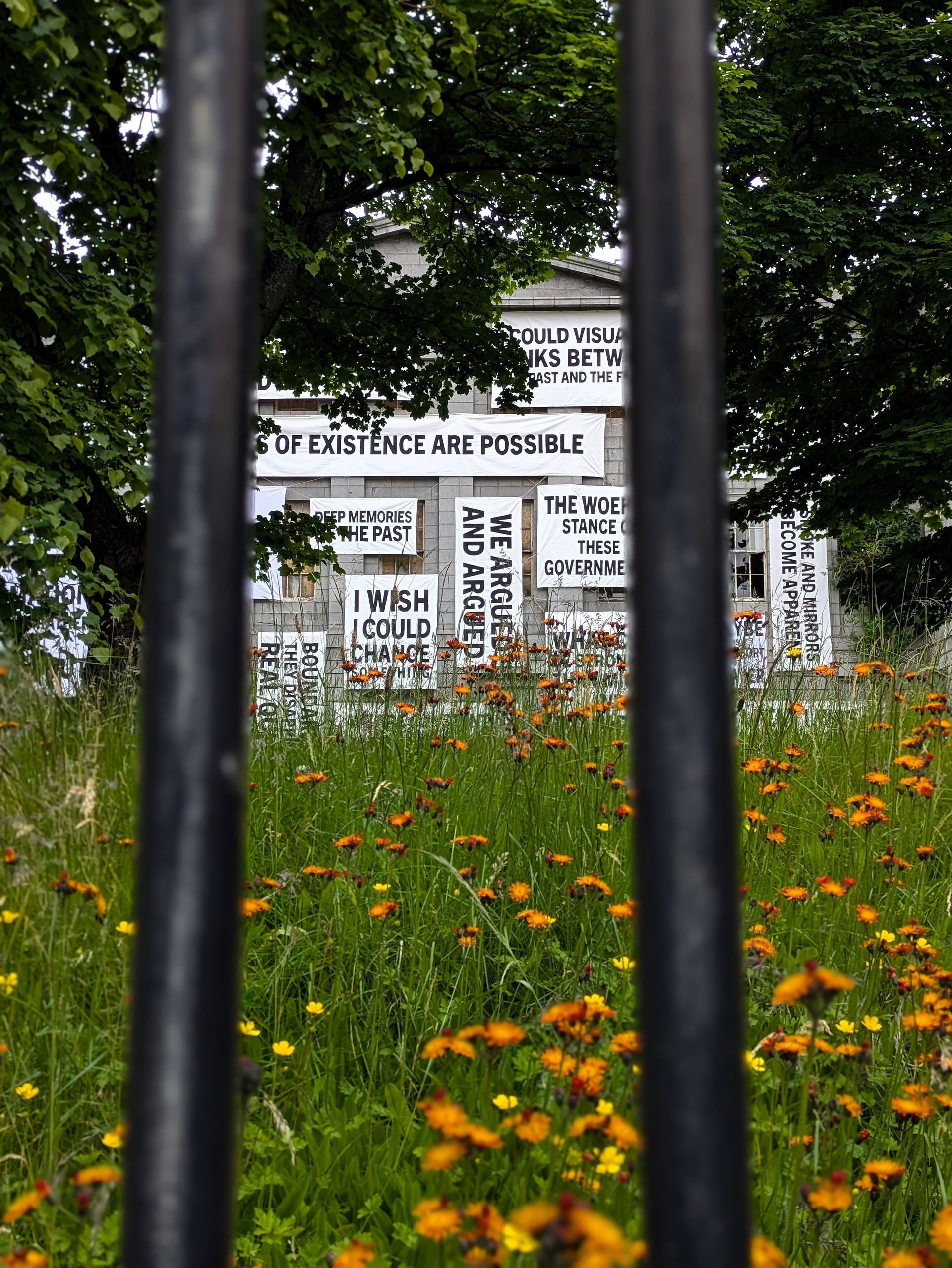 One of the Aberdeen street art murals on a building depicting poster statements, with greenery around the building.