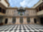 A view of the Peacock Courtyard within the palace. Intricate designs on the walls and a black and white chequer floor. Attractions You Should Visit in Udaipur, India