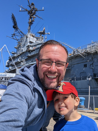 Father and son in front of a huge aircraft carrier at dockside visited during a family day out in the East Bay region.