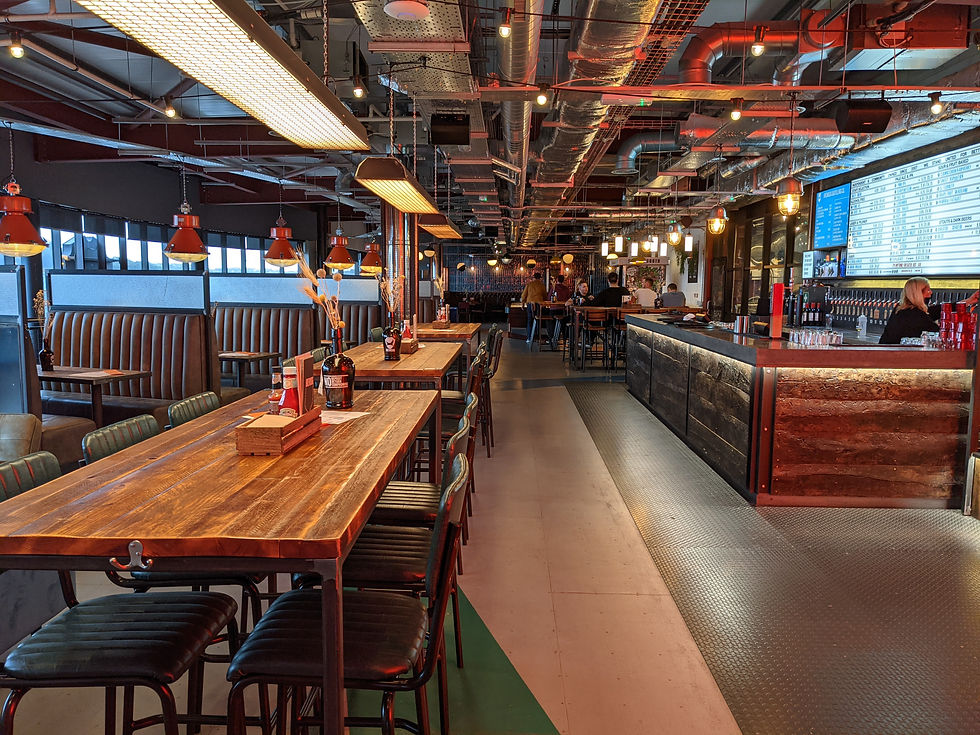 Modern industrial restaurant interior with wooden tables, hanging lights, seated patrons, and bright menu boards at the bar. Things to do in Aberdeenshire.