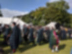 Men in tartan kilts march with spears at an outdoor Highland gathering under tents and trees on a sunny day. Things to do in Aberdeenshire.