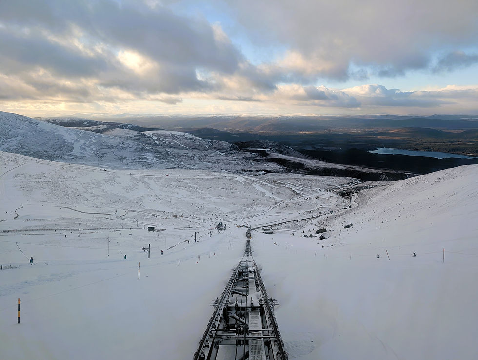 Snowy mountain landscape with ski tracks, winding roads, and distant lakes. Cloudy sky with sunlight breaking through, creating a serene mood. Things to do at Aviemore in Scotland