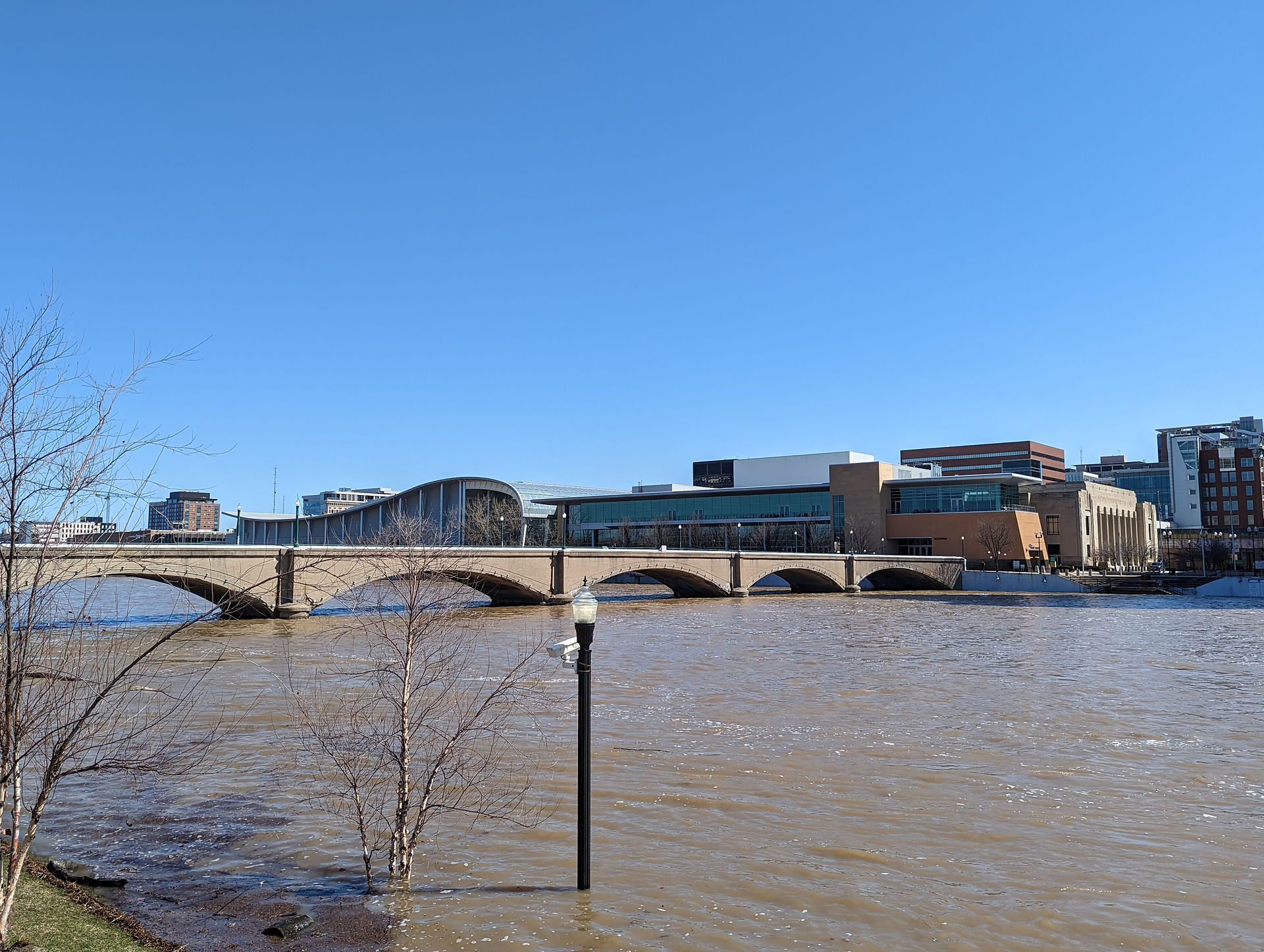 Large swollen river flowing under a bridge, with large buildings on the riverbanks, seen during a family day out in Grand Rapids