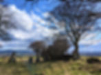 Leafless trees and standing stones on a grassy hill under a blue, cloudy sky, with distant valleys and mountains. Things to do in Aberdeenshire.