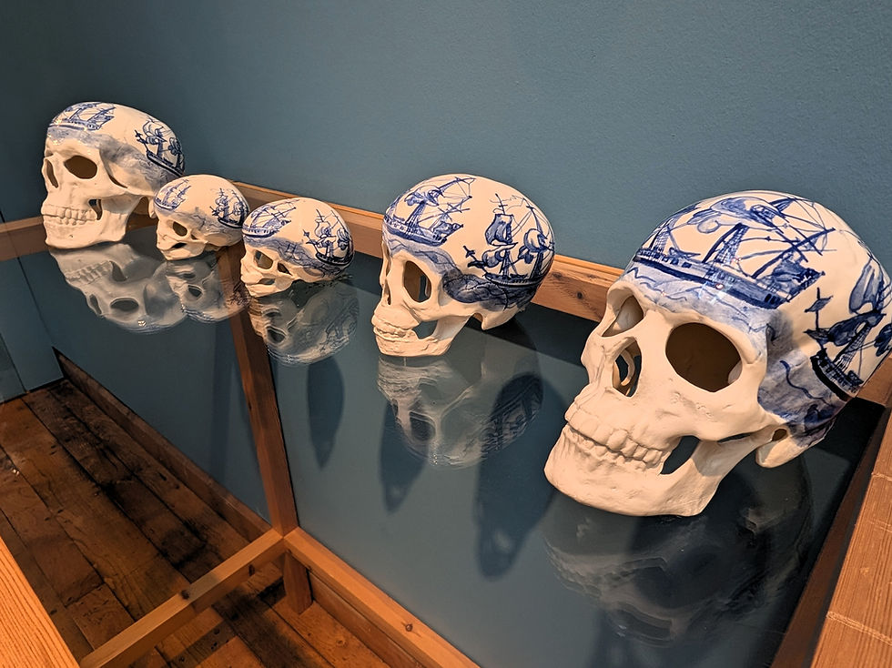 Line of ceramic skulls with blue nautical designs, reflecting on a glass table. Blue wall background, wooden floor and edges. Calm setting. Things to do in Glasgow Scotland.