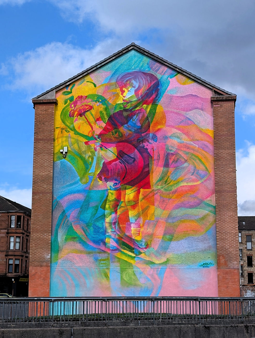 Colorful mural of a child and flowers on a building wall, set against a blue sky. Bright, vivid hues create a joyful atmosphere. The street art murals of Glasgow.