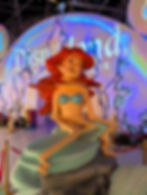 Distorted Ariel statue with red hair and blue seashell top in a Disney display, lit by neon projections and castle outlines. Street Art Murals of London