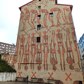 Street art murals on the gable end of a building depicting a series of full skeletons.