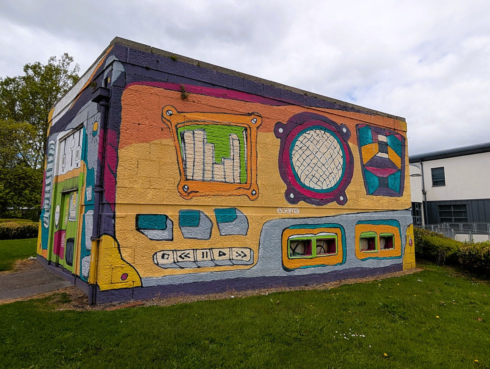 Colorful mural on a small building shows abstract retro-style panels and shapes in orange, purple, teal, and yellow under a cloudy sky. Street art murals of Aberdeen.