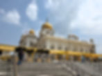 People walking up steps toward a marble building with golden domes, under a partly cloudy sky. Yellow awnings line the walkway. Tourist places to visit in Delhi.