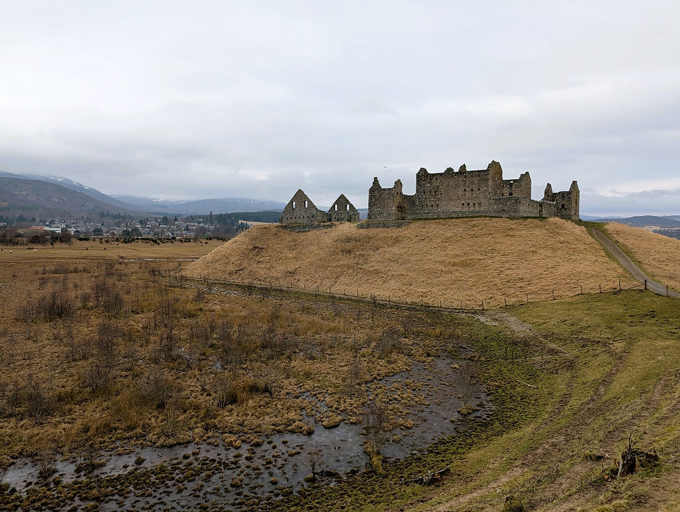 Ruined stone castle on a grassy hilltop, surrounded by brown marshy fields. Overcast sky and distant town in the background. Mood is serene. Things to do at Aviemore in Scotland.