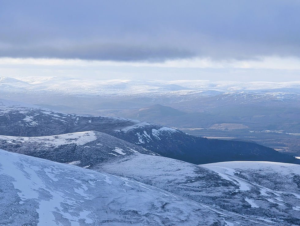 Snow-covered hills under a cloudy sky, with distant mountain ranges. The scene conveys a calm, serene winter landscape. Things to do at Aviemore in Scotland.