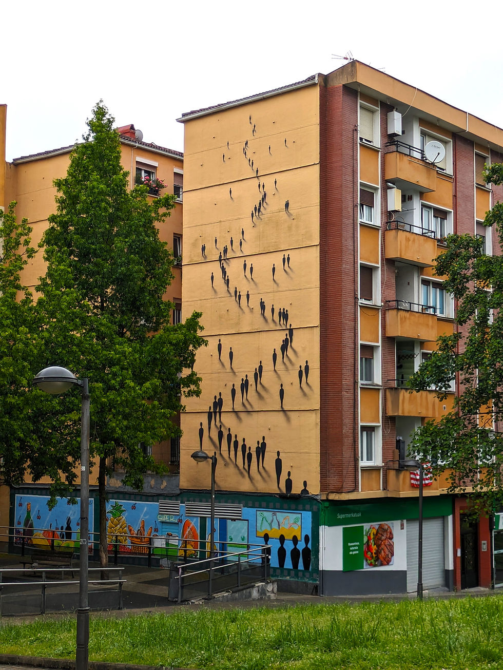 Murals of silhouettes climb a building under a cloudy sky. Bright fruit and vegetable paintings decorate the lower wall. Urban setting. The Street Art Murals of Bilbao