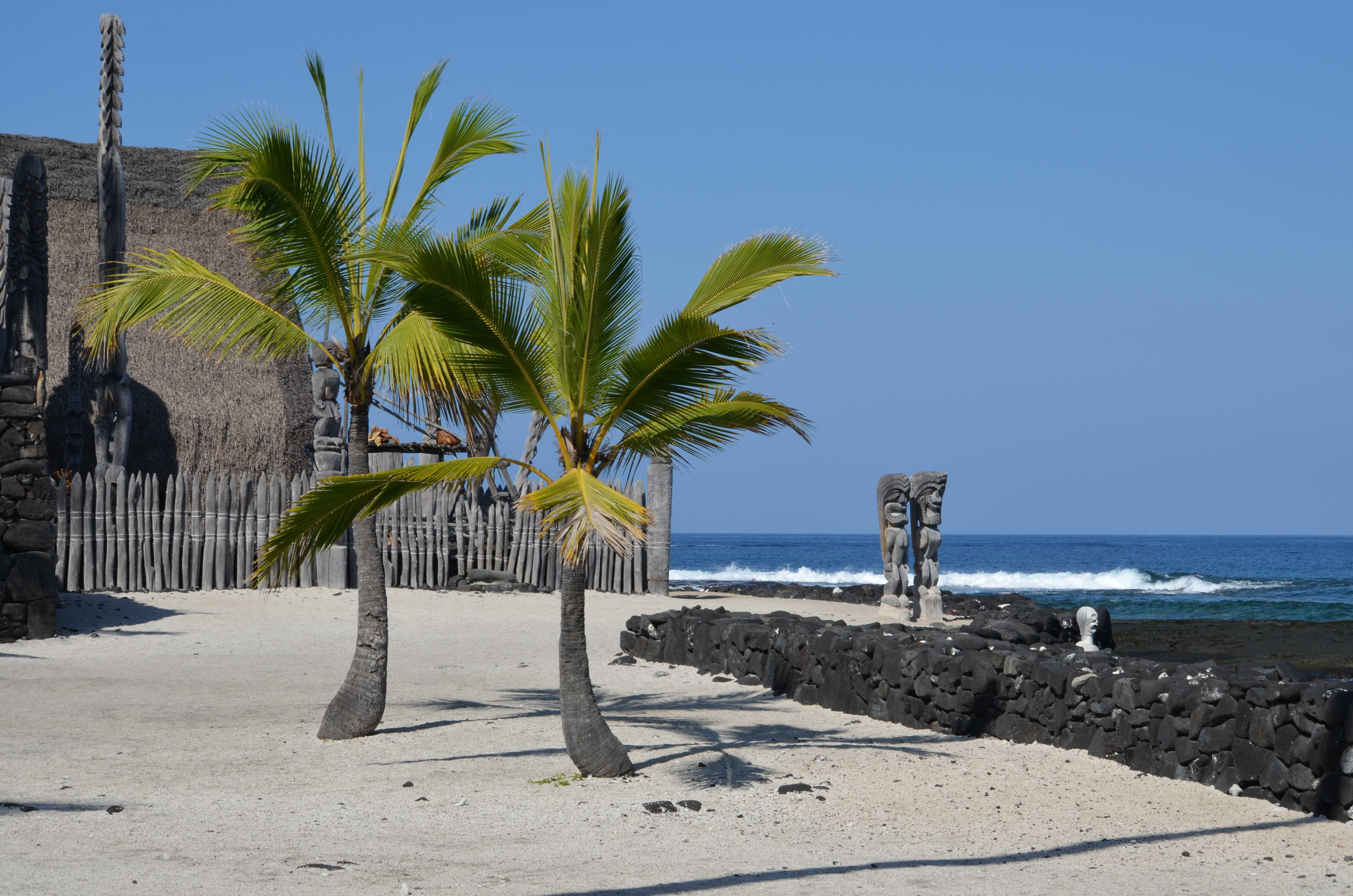 Palm trees on a sandy beach with stone statues and a rock wall