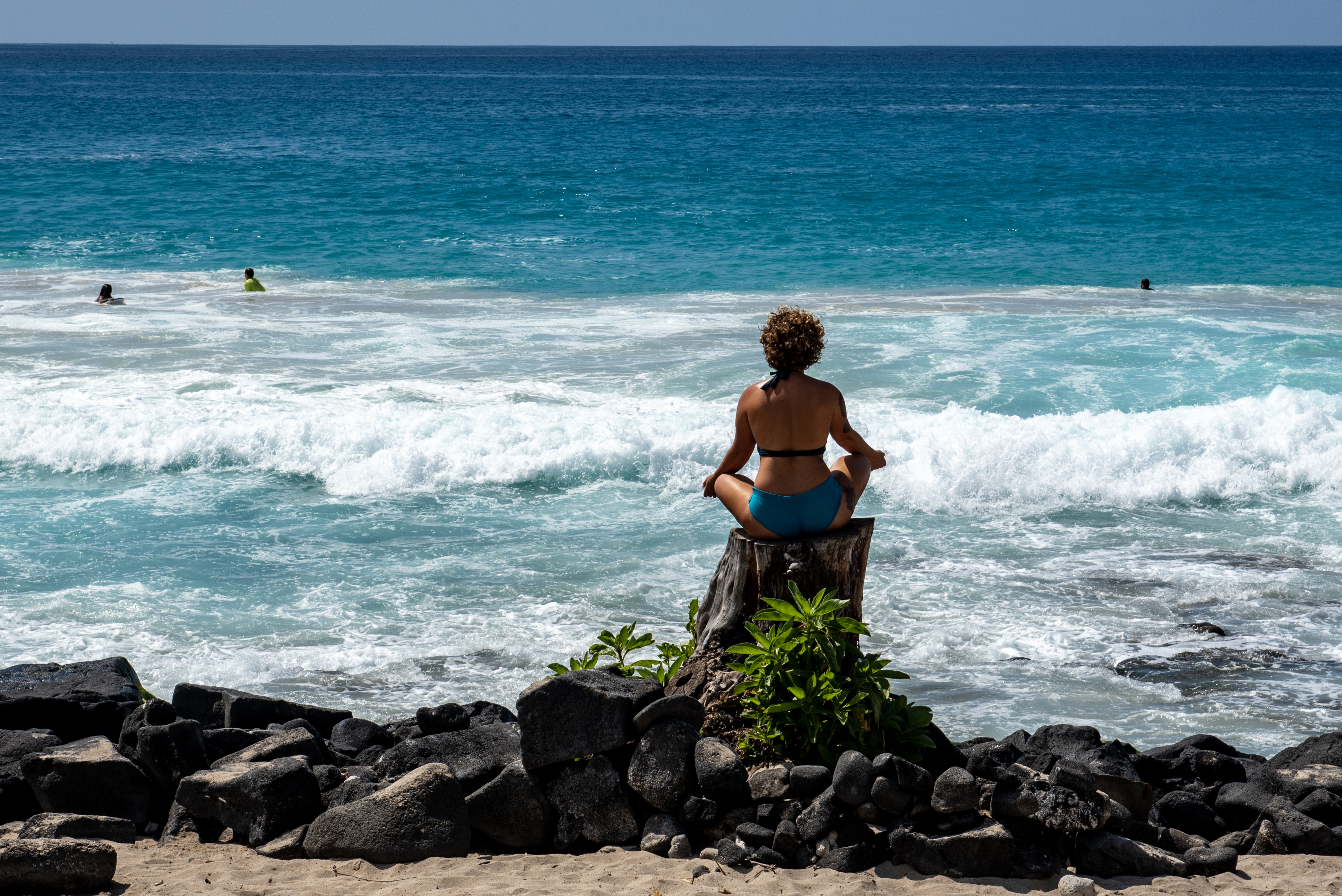 Person sitting on beach rock facing the ocean