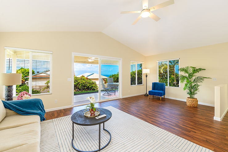Bright modern living room with cream sofa, blue chair, wood floor, plants, ocean-view windows, and sliding glass door to patio