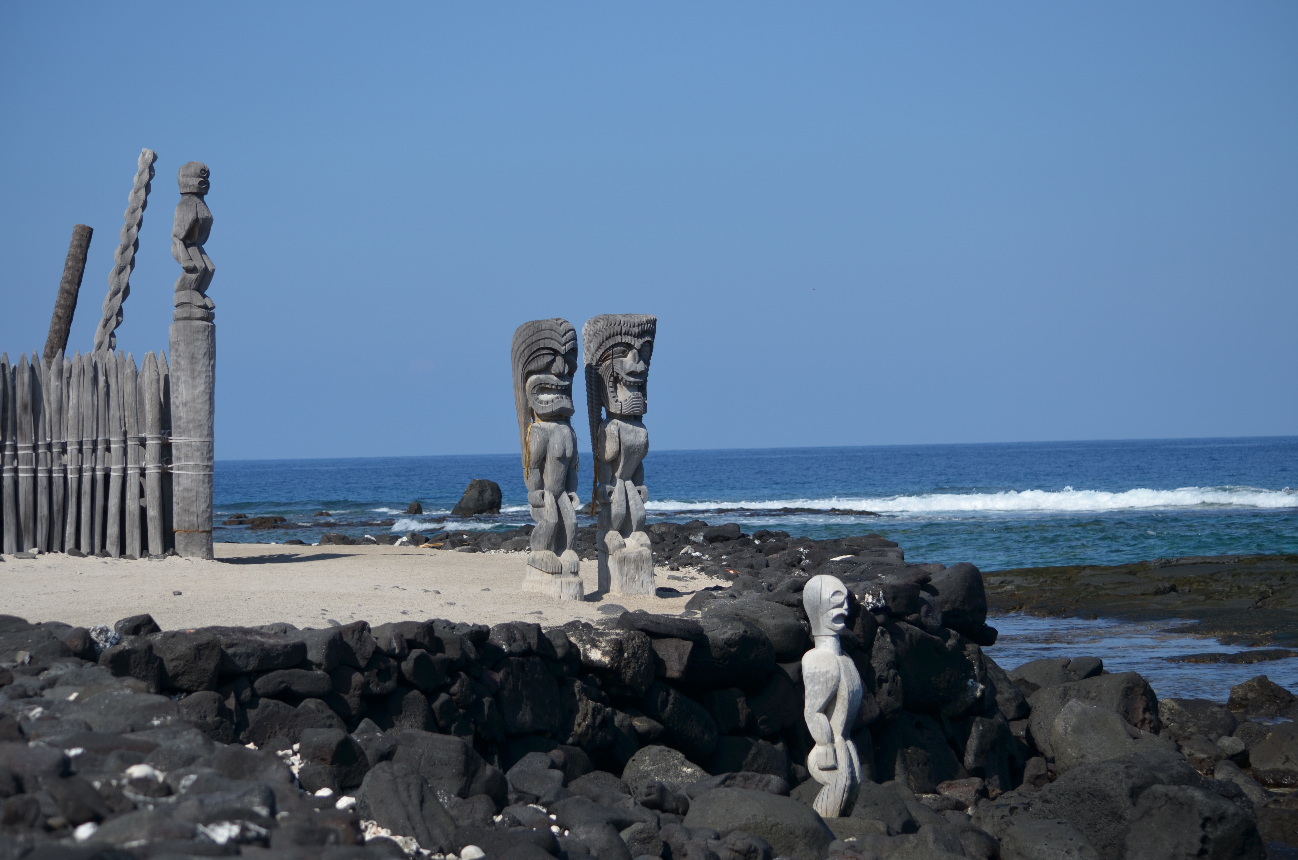 Stone tiki statues on rocky shoreline with ocean