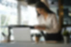 A writer in a white shirt with long dark hair leans over her laptop with marketing notes in her hand.