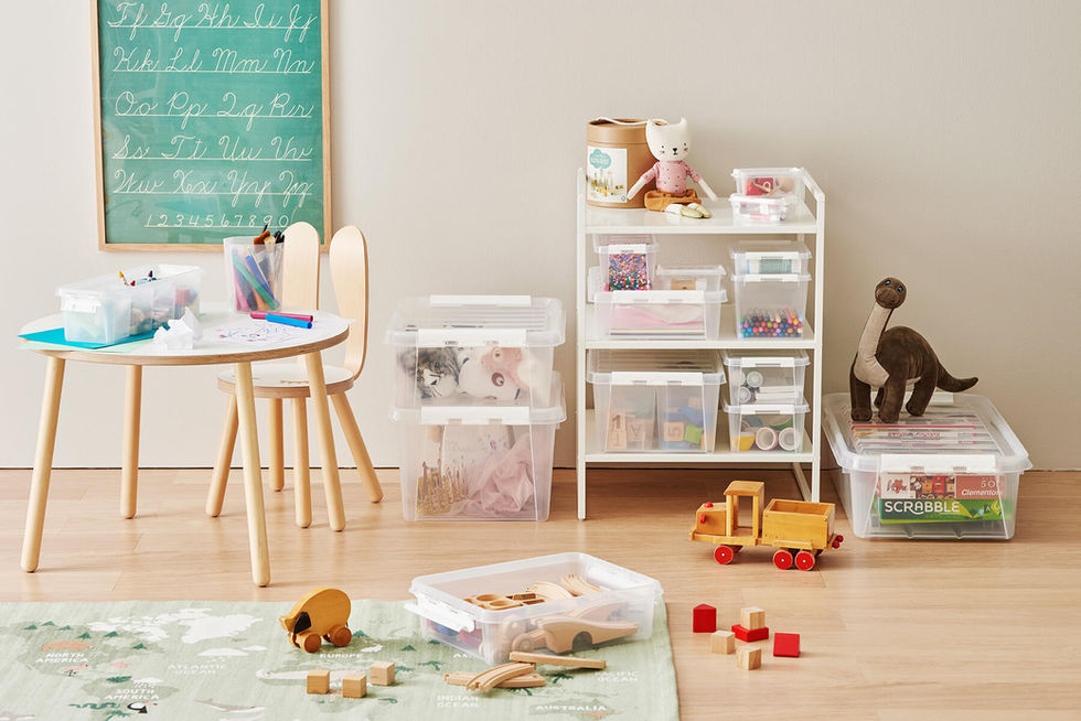 Opbergboxen met witte clips in kinderkamer met speelgoed, open box met houten treinset op vloerkleed en schoolbord aan muur