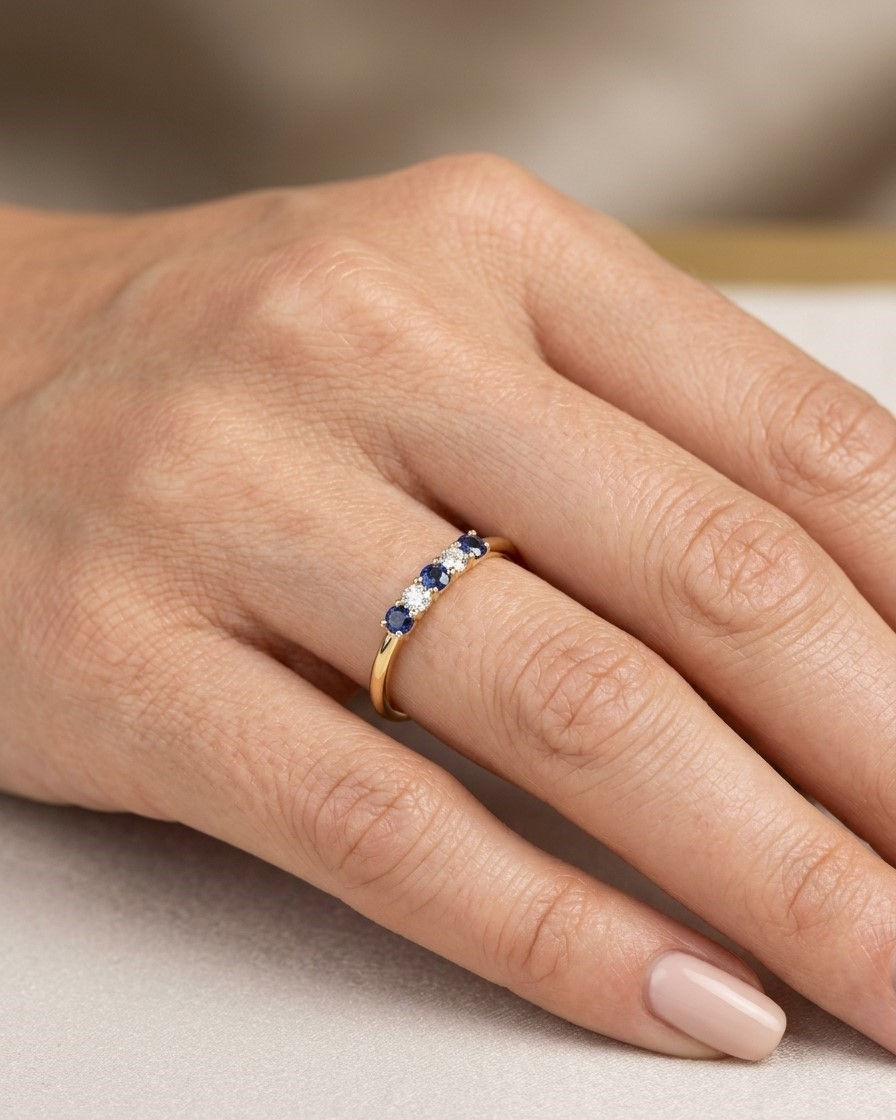 Grande plano de uma mão elegante a usar um anel em ouro amarelo de 19.2kt com 3 safiras intercaladas com 2 diamantes.