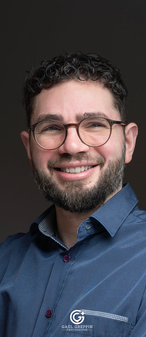 Portrait professionnel d'un homme souriant, lunettes, barbe, logo photographe.