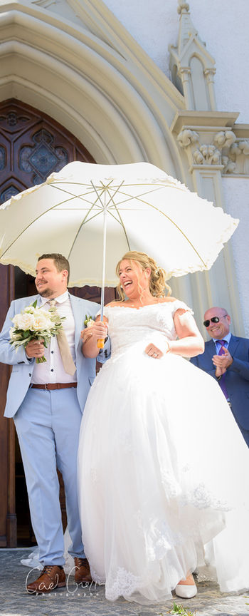 Jeune couple quitte l'église après leur mariage, portant un parapluie. Photographe mariage