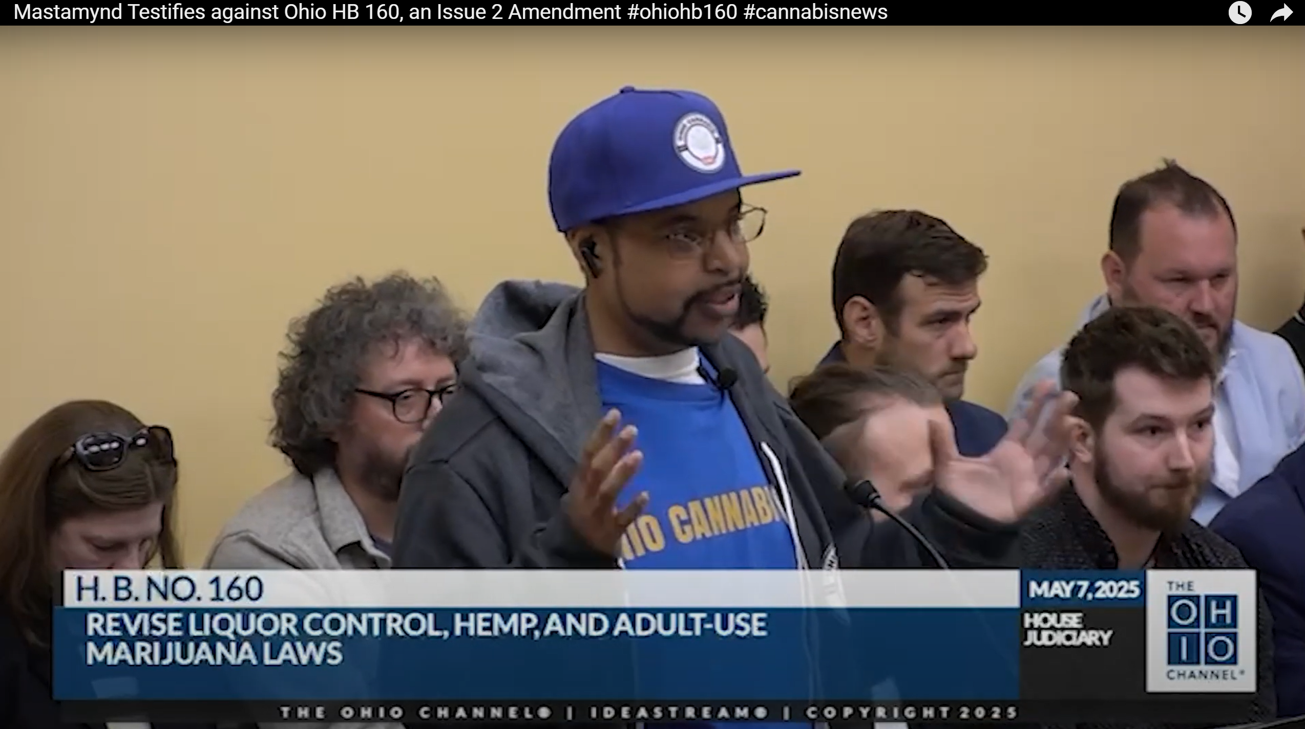 Anthony D Riley aka Mastamynd from Ohio Cannabis Live in a blue cap and "Ohio Cannabis Live" shirt speaks at a hearing. Background shows audience; text on screen: H.B. NO.160, May 7, 2025. House Judiciary.