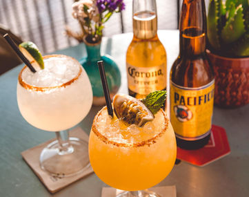 Two Mexican beers and two cocktail glasses filled with Margarita and the famous Taco Paco Passionfruit Margarita on a table on the Taco Paco veranda