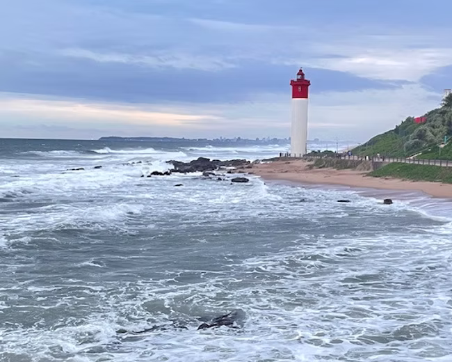 Ein rot-weißer Leuchtturm steht fest auf einem dunklen Felsen, während mächtige, stürmische Meereswellen dagegen peitschen. Das Bild symbolisiert den Weg der Wahrheit, die Bergpredigt als göttlichen Schutzraum und das unerschütterliche Fundament Gottes im endzeitlichen Sturm.